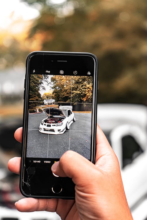 Person mit Smartphone neben dem beschädigten Fahrzeug